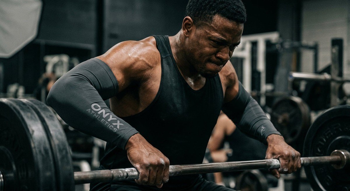 Close-up of a professional athlete wearing supportive compression sleeves while lifting heavy weights, highlighting muscle texture and intensity.