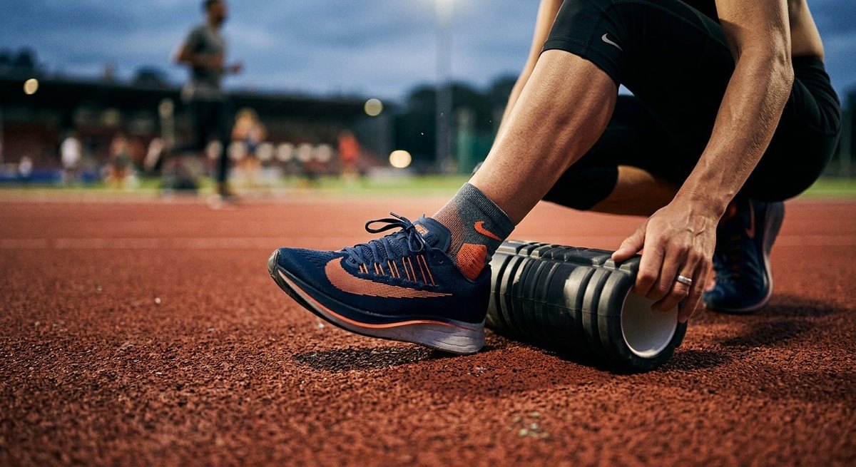 Close-up of a runner's foot using a massage roller tool on a textured track surface under dramatic high-speed action photography lighting
