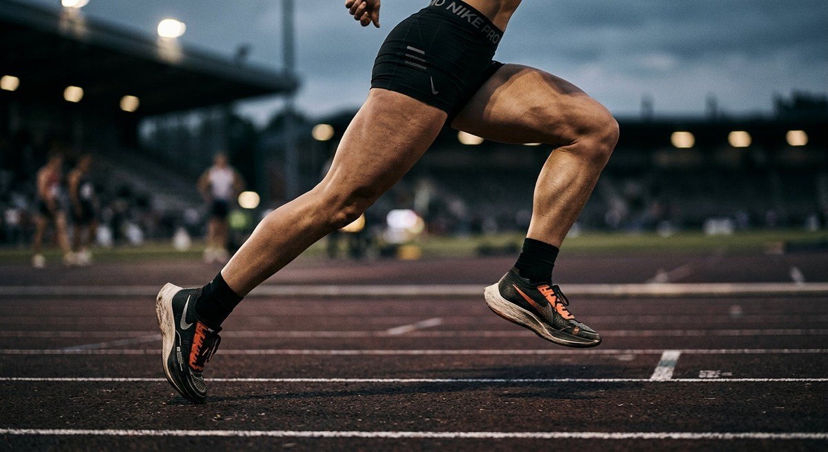 Close-up of a runner's legs in mid-stride on a track, featuring sharp fine details and high-contrast moody athletic photography.