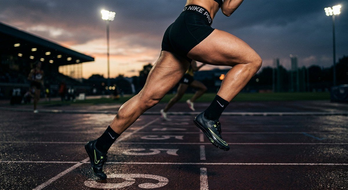 Close-up of a runner's legs mid-stride on a track, emphasizing muscular detail and high-contrast, moody atmospheric lighting