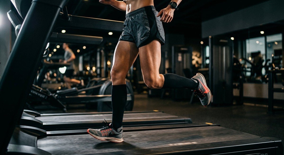Close-up of a runner's legs on a treadmill wearing high-performance moisture-wicking shorts with dramatic cinematic lighting.
