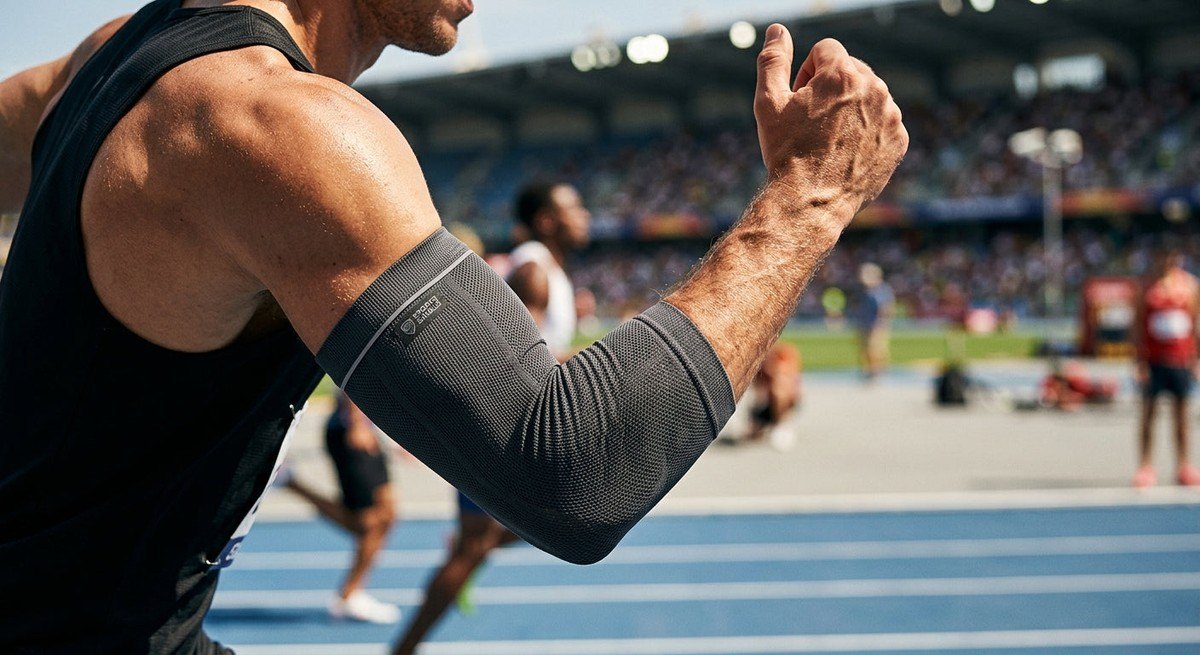 Close-up of a runner's muscular arm wearing a technical UV-protective sleeve, highlighting fine fabric texture under intense stadium-like sunlight.
