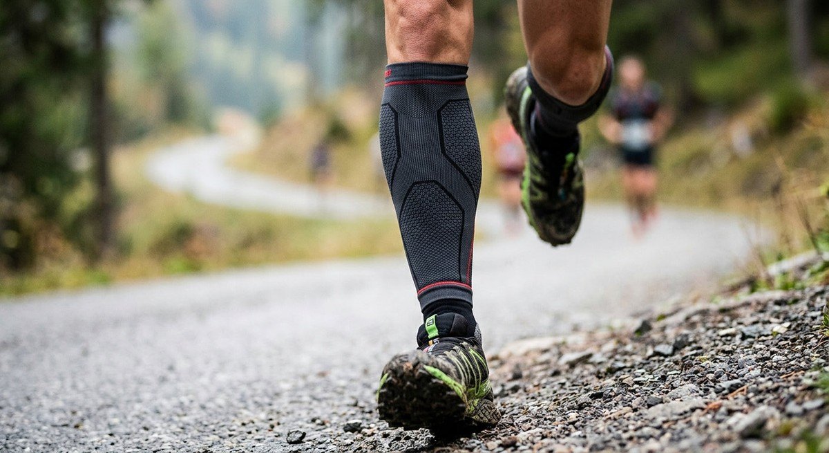 Close-up of a runner wearing high-performance compression leg sleeves, highlighting the technical fabric texture and precision fit during an aggressive downhill stride.