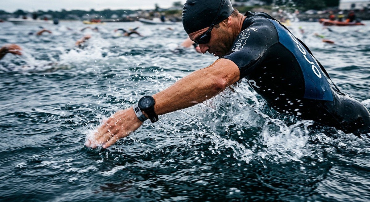 Close-up of a swimmer's arm entry during an open water race, showing high-speed motion blur and the sleek texture of professional triathlon gear.
