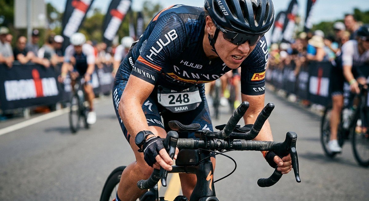 Close-up of a triathlete's hands on a road bike handlebar during a competitive race, showing sharp focus and intense expression.