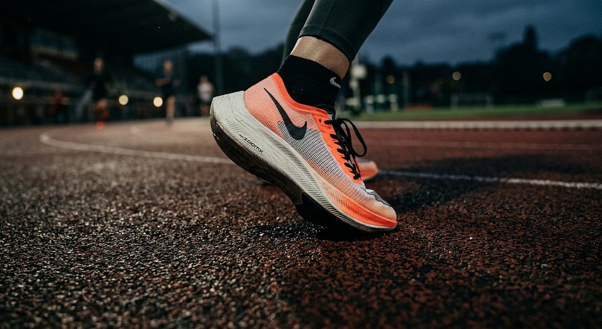 Close-up of elite athletic footwear touching a synthetic running surface, showing realistic textures of the foam midsole and carbon plate, with a moody, cinematic atmosphere.