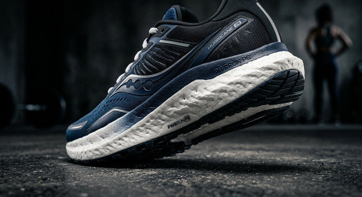 Close-up of Saucony Hurricane 26 footwear showing detailed texture of the dual-density foam midsole in a moody, high-contrast studio setting.