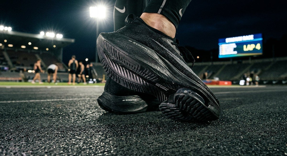 Close-up of the carbon-infused plate and textured foam midsole of a high-performance racing shoe with cinematic stadium lighting.