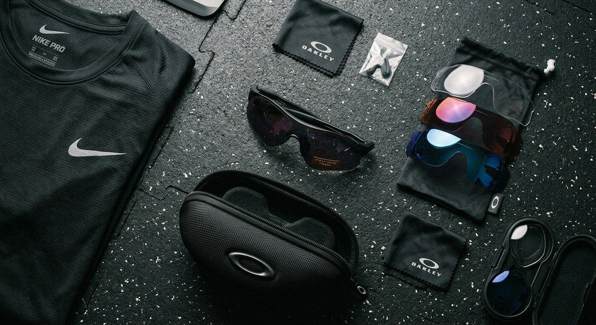 Detailed flat-lay of premium sports eyewear, including interchangeable lenses and a protective hard case, set against a dark, textured athletic surface.