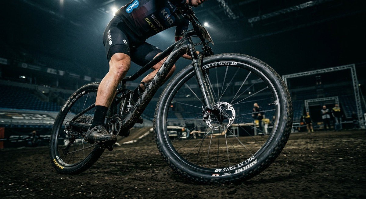 Dramatic cinematic lighting illuminating a professional cyclist's mountain bike wheel in a dark, moody stadium, capturing the metallic texture and the kinetic blur of the spokes.