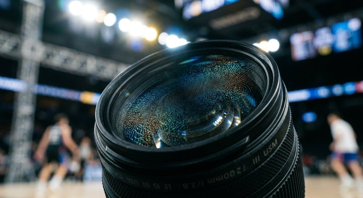 Macro close-up of advanced lens material showing anti-reflective coating texture under cinematic stadium lights.