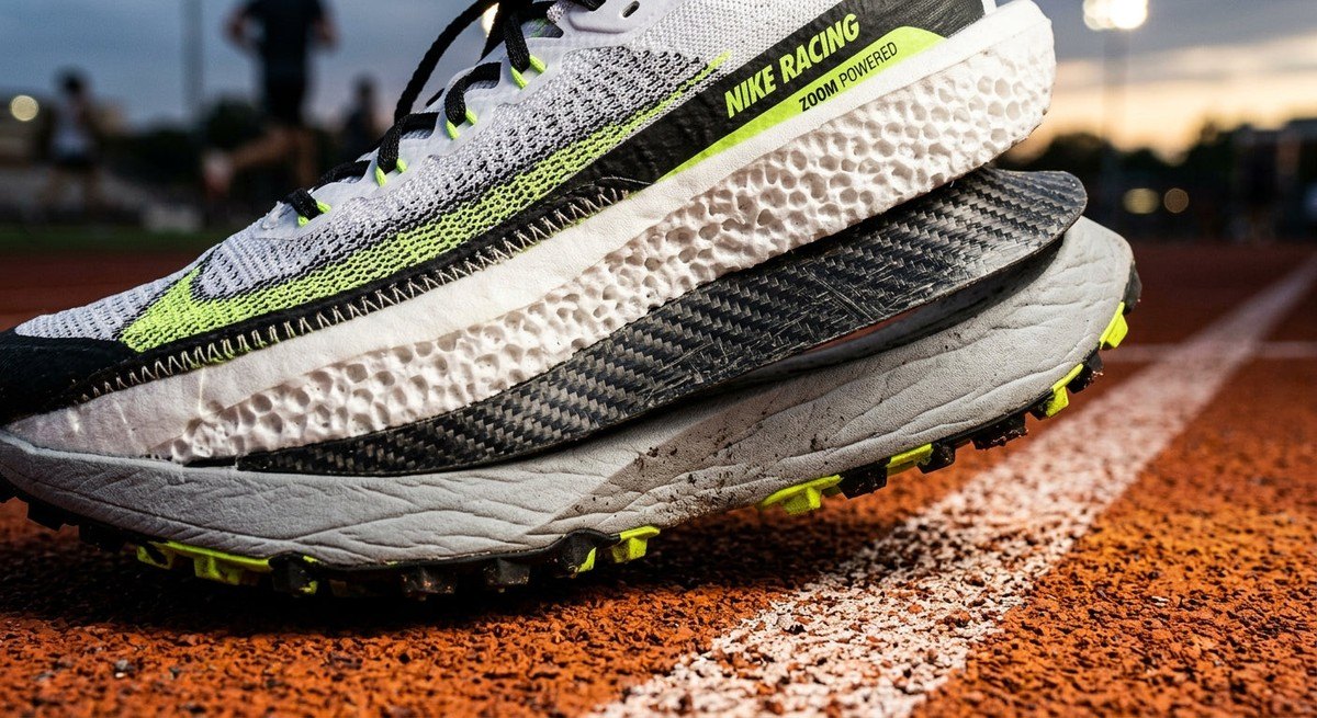 Macro detail of the advanced midsole foam and carbon-fibre plate architecture of a racing shoe, highlighting the intricate material textures and engineering precision.