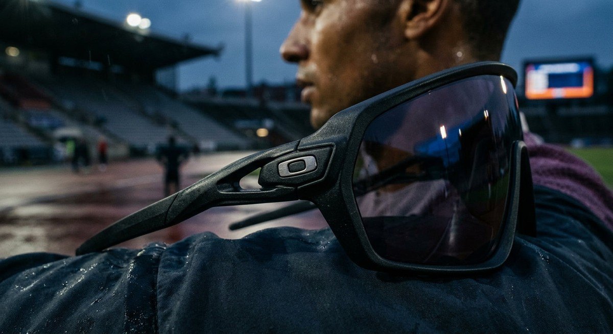 Macro photography of the Oakley Plantaris SQ frame showing the intricate O-Matter material texture and aerodynamic lens geometry under moody stadium lighting.