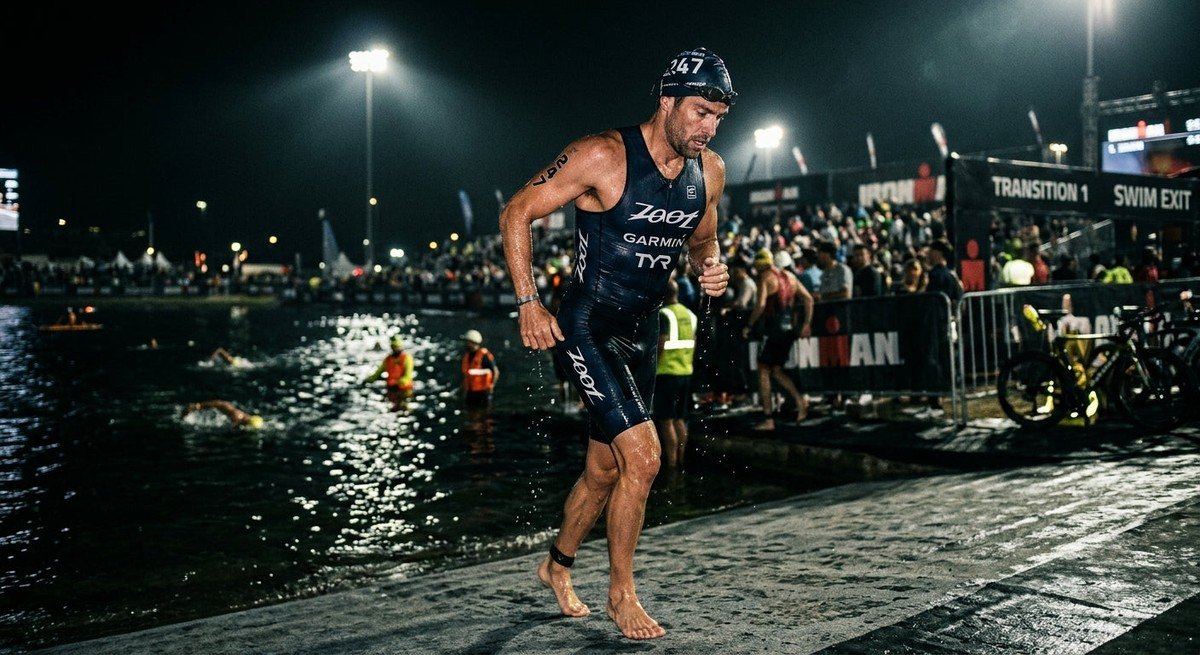 Moody cinematic shot of a triathlete transitioning from a swim, with water droplets on skin and dramatic stadium lighting.