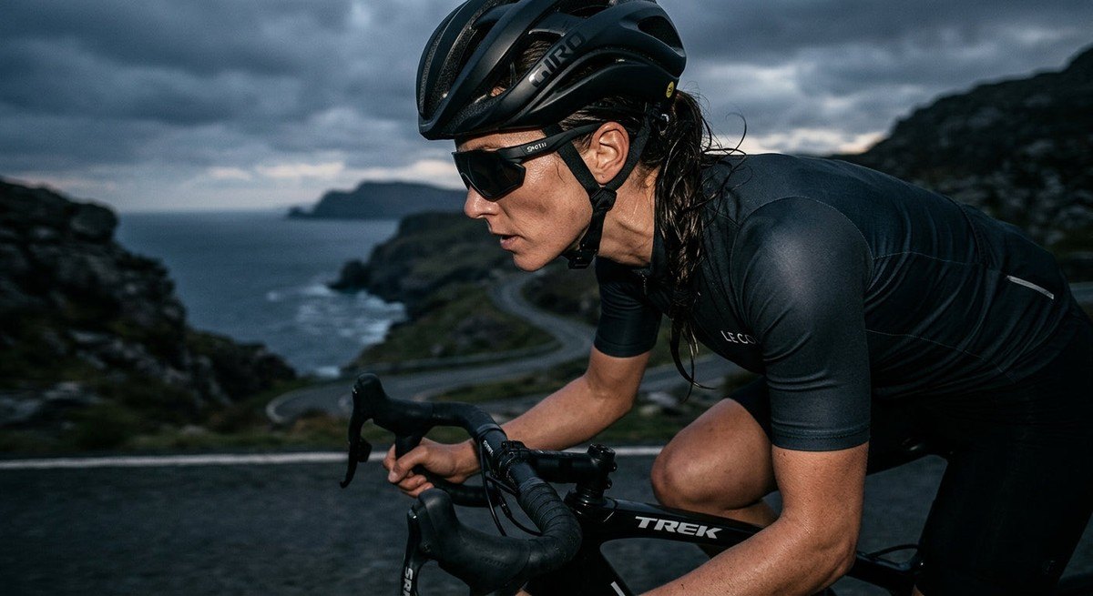 Moody, high-contrast photography of a cyclist's profile, showcasing the perfect alignment and grip of performance sunglasses designed for a smaller facial structure.