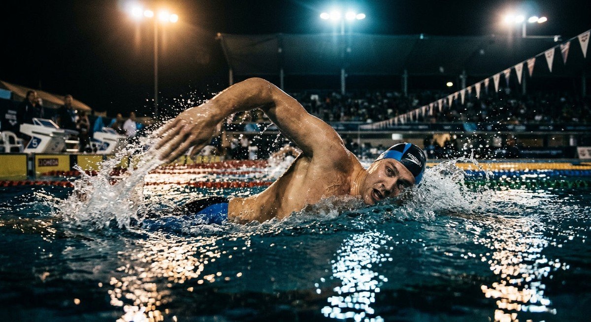 Professional athlete mid-stroke, capturing water droplets and motion blur under dramatic stadium lighting.