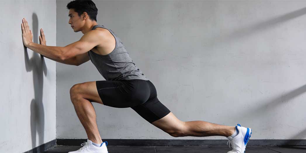A runner performing a bent-knee calf stretch against a wall to target the soleus muscle and relieve tension on the shin bone.