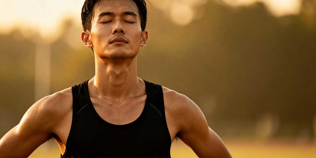 A runner practicing the physiological sigh breathing technique post-workout, standing with eyes closed to down-regulate the nervous system and shift into recovery mode.