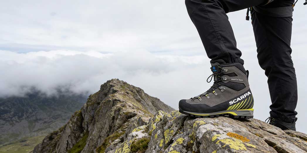 A mountaineer wearing Scarpa Manta Tech boots standing on a exposed rocky ridge in Snowdonia with moody clouds in the background.