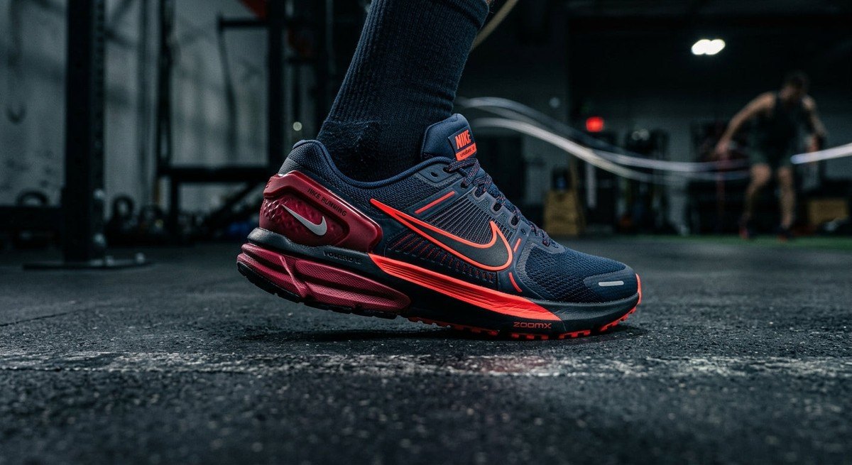 Side profile view of the Nike Vomero Premium, showcasing the aggressive heel counter and vibrant Bright Crimson colour accents in dramatic lighting.