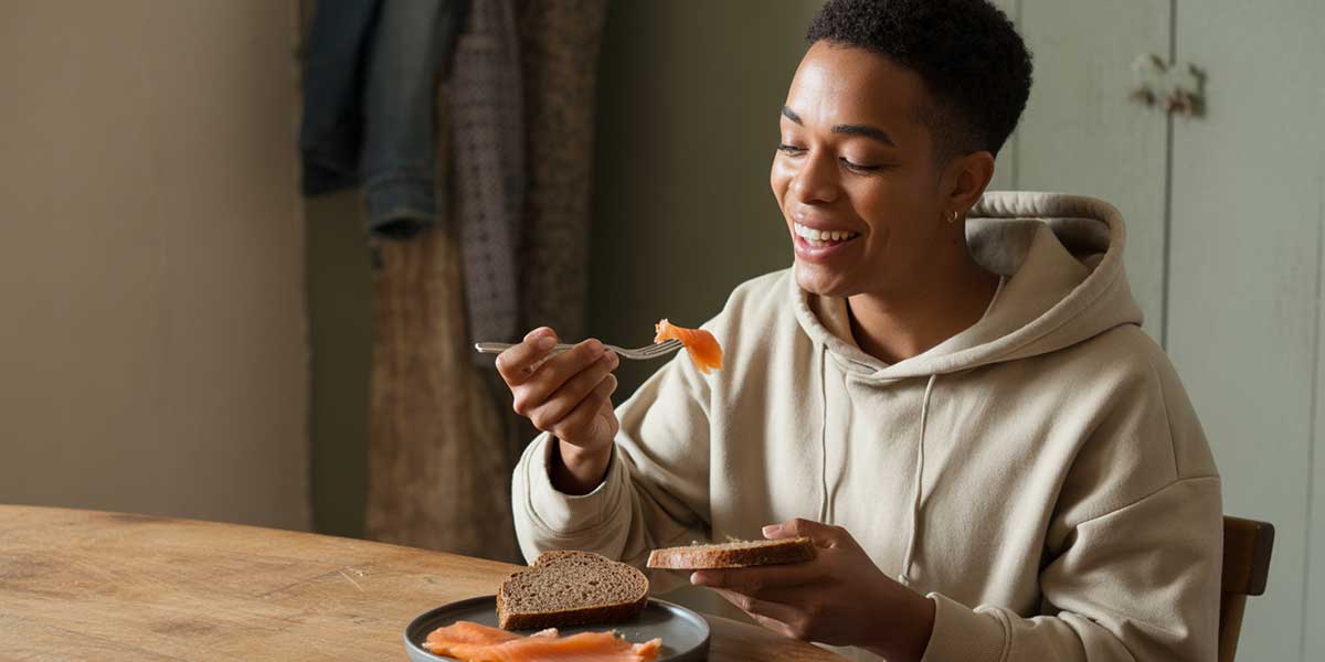 A person in Sundried activewear eating a healthy savoury breakfast of smoked salmon on rye bread.