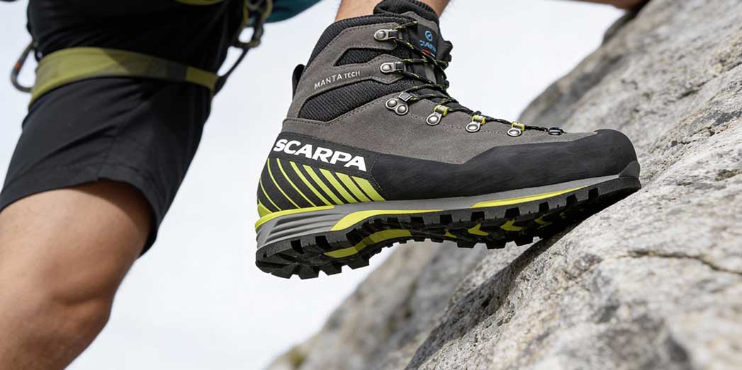 A climber high-stepping onto a granite ledge demonstrating the grip and stiffness of B2 mountaineering boots on technical rock.