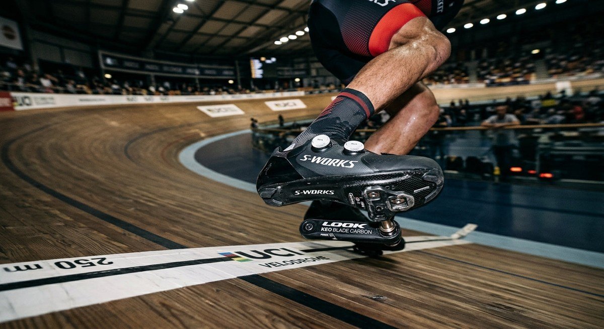 Top-down view of a cyclist's shoes and pedals in a velodrome setting, highlighting the precision engineering of modern power measurement hardware